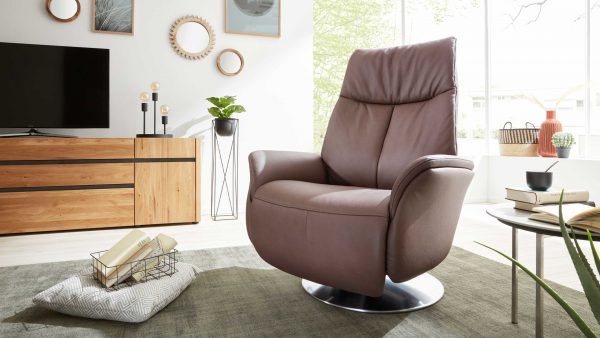Modernes Wohnzimmer mit dem Interliving Sessel Serie 4550 - Sessel 37O44 brauner Lederdrehsessel auf grünem Teppich, Holzsideboard, TV, dekorativen Spiegeln, Topfpflanzen, Büchern und einem großen Fenster, das natürliches Licht hereinlässt.