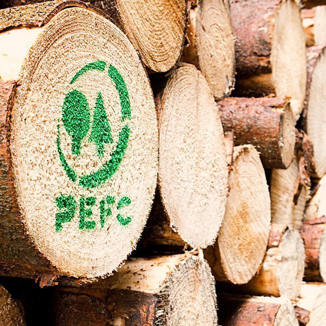 Gestapelte Stämme, wobei ein Stamm ein grünes PEFC-Logo und einen Text aufweist, der auf die Zertifizierung der nachhaltigen Forstwirtschaft hinweist.